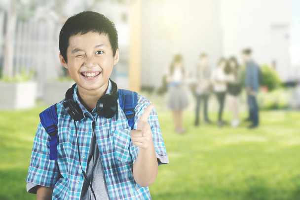Retrato de un estudiante preadolescente guapo señalando y guiñando el ojo a la cámara mientras está de pie con sus amigos en el parque
 - Foto, imagen