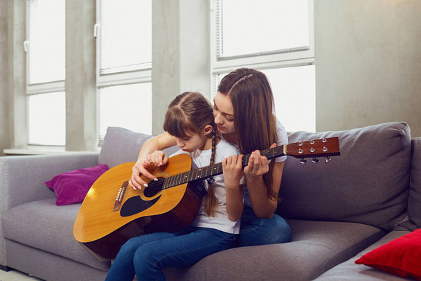 Mom plays guitar together with teenage daughter at home. - Fotó, kép