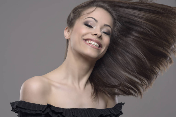 Zatrzymany ruch wietrznie latające włosy piękną kobietę przed studio szary tło. - Zdjęcie, obraz