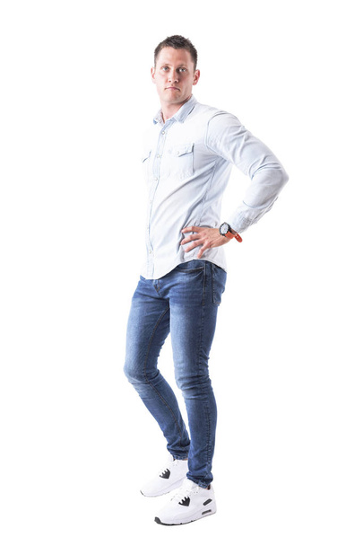Handsome young adult caucasian blue eyed man in light blue shirt looking at camera with hands on hips. Full body isolated on white background. - Foto, Imagem