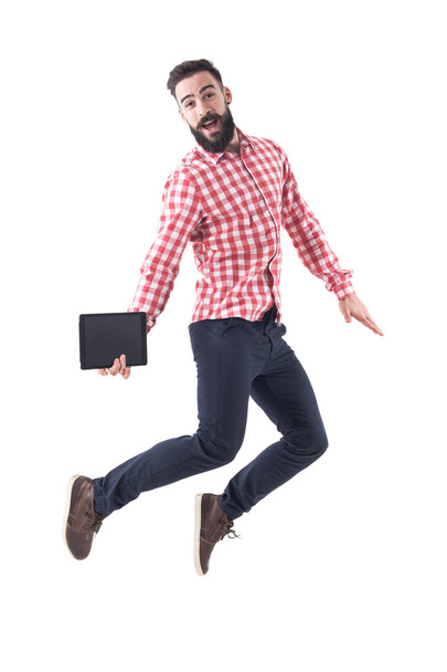 Successful excited young business man holding tablet jumping in mid air with open mouth. Full length isolated on white background. - Fotó, kép