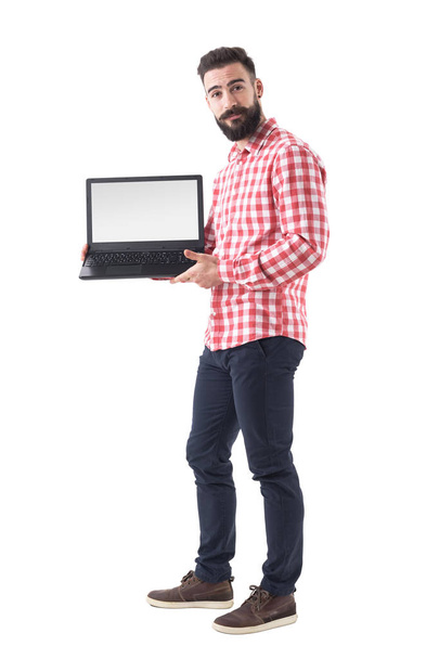 Hűvös szakállas csípő srác intelligens alkalmi ruhák üres laptop monitor mutatja. Teljes hossza elszigetelt fehér background. - Fotó, kép
