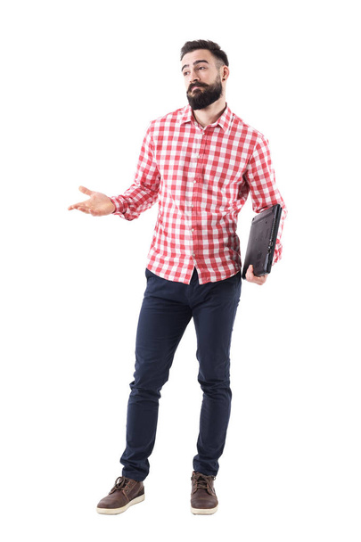 Confused young adult bearded business man with laptop under arms shrugging and looking away. Full body isolated on white background. - Foto, imagen