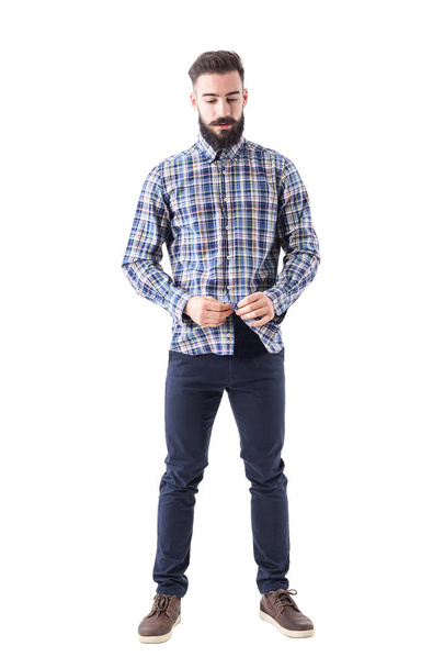Relaxed cool bearded hipster buttoning plaid checkered shirt looking down. Full body isolated on white background. - Foto, Imagem