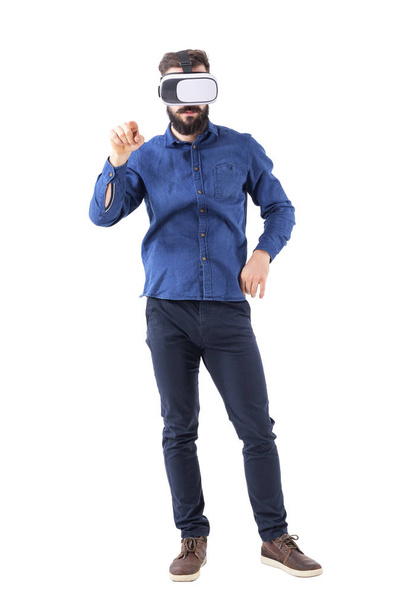 Вид спереди бизнесмена в VR очках, указывающий пальцем на интерактивный сенсорный экран. Полное тело изолировано на белом фоне
. - Фото, изображение