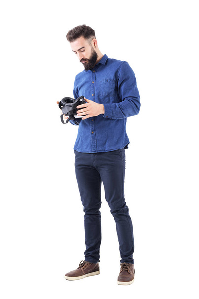 Serious business man holding and checking virtual reality glasses headset. Full body isolated on white background. - Φωτογραφία, εικόνα