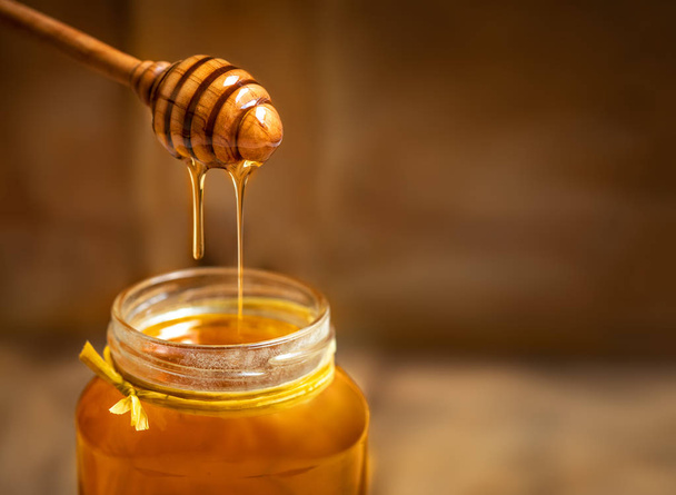 Honey in a glass jar with honey dipper on rustic wooden table background. Copy space.  - Foto, imagen