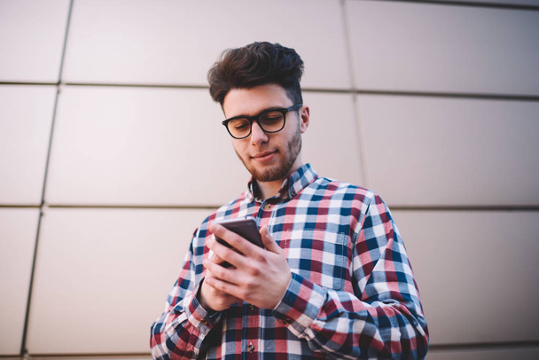 Positive hipster guy in trendy shirt using smartphone for chatting in social networks with friends ,handsome young man share multimedia content in blog using 4G connection and telephone apps - Photo, Image