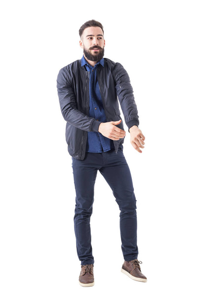 Homem barbudo jovem se vestindo atingindo manga jaqueta bombardeiro olhando para longe. Corpo inteiro isolado em fundo branco
. - Foto, Imagem