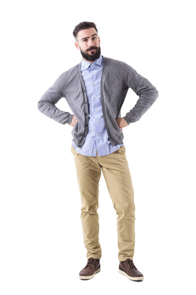 Skeptical young fashionable bearded man with arms on hips looking at camera. Full body length portrait isolated on white studio background. - Photo, Image