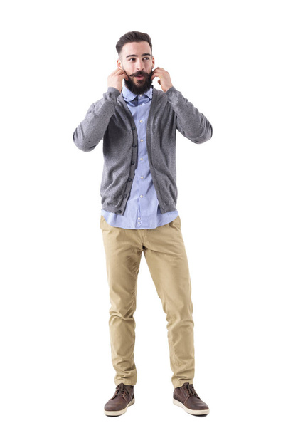 Cool relaxed funky hipster in cardigan adjusting mustache and looking away. Full body length portrait isolated on white studio background. - Zdjęcie, obraz