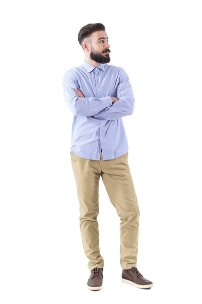 Confused young bearded business man with crossed hands looking away. Full body length portrait isolated on white studio background. - Photo, Image