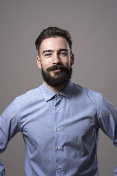 Vertical headshot of proud successful confident bearded businessman with arms on hips smiling at camera against gray studio background. - Photo, Image