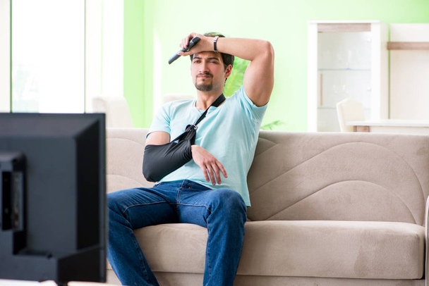 Bras blessé assis sur le canapé regarder la télévision - Photo, image