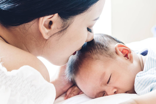 Mutter küsst und hält schlafendes Baby an der Hand auf weißem Bett - Foto, Bild