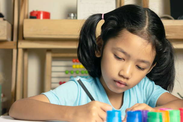 Το μικρό κορίτσι γράφει ένα βιβλίο με πολύ πυκνό. Ομάδα χρωμάτων που βάζουν στο τραπέζι. - Φωτογραφία, εικόνα