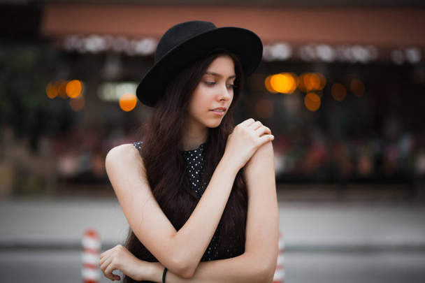 Tender brunette woman wearing hat and vintage dress posing at the city street with lights  - Photo, image