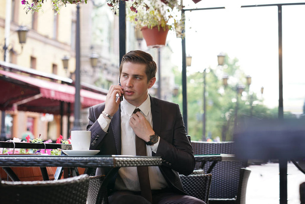 Молодой бизнесмен пришел на обед в уличное кафе, он неодобрительно эмоционально разговаривал по телефону
 - Фото, изображение