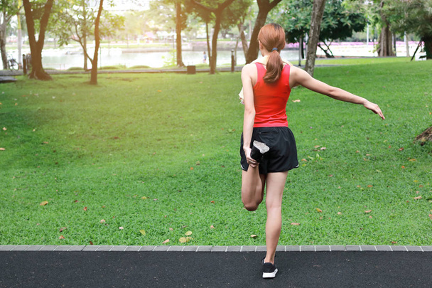 Vue arrière de la femme asiatique en bonne santé étirant ses jambes avant de courir dans le parc. Concept de fitness et d'exercice
. - Photo, image
