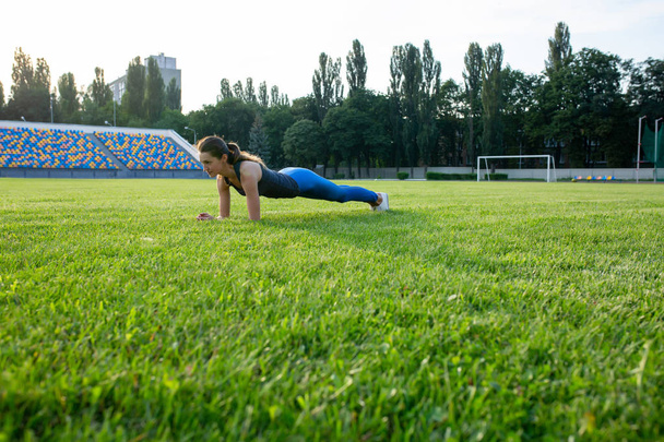 Fit brunette woman doing plank exercise outdoor at the stadium - Photo, Image