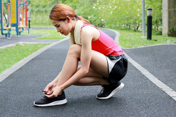 Side view of healthy Asian woman tying shoelaces on running shoes on the street. Fitness and workout wellness concept. - Foto, immagini