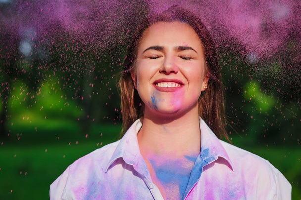 Funny caucasian woman posing with closed eyes with exploding around pink Holi paint  - Photo, Image
