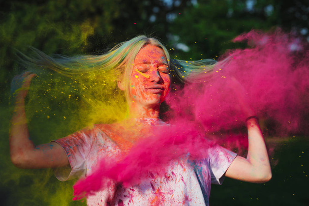Mulher nova surpreendente com cabelo voador posando com tinta Holi amarelo e rosa explodindo
 - Foto, Imagem