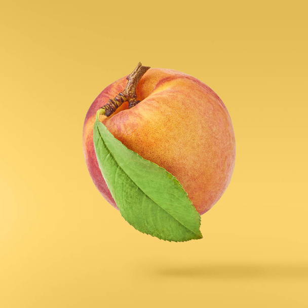 新鮮な熟した桃を黄色の背景に分離された緑の葉に飛ぶ。食品浮上、高解像度画像の概念 - 写真・画像