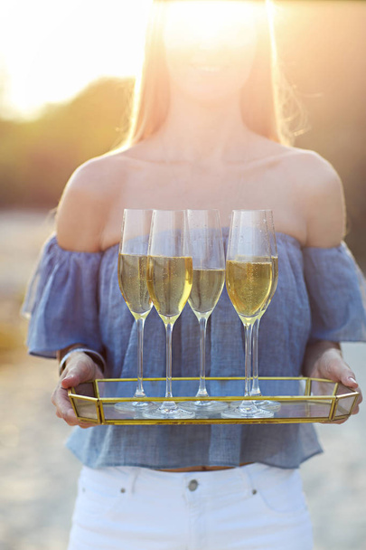 Happy woman holding tray with champagne sparkling wine into glasses outdoors at a beach. Sunset beach party - Photo, Image