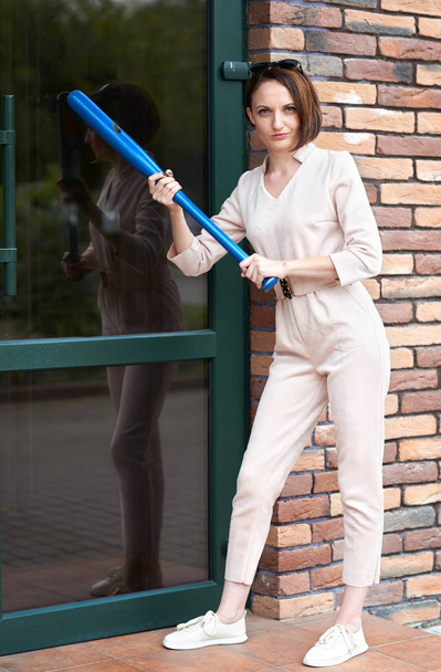 la fille se tient à la porte fermée du magasin et tente de le casser avec une batte de baseball
 - Photo, image