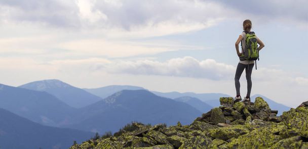 Πίσω όψη του λεπτή κοπέλα με Σακίδια στέκεται πάνω σε βραχώδες βουνό κορυφή ενάντια φωτεινό μπλε ουρανό πρωί απολαμβάνοντας ομίχλη οροσειρά Πανόραμα. Τουρισμός, ταξίδια και υγιή τρόπο ζωής έννοια. - Φωτογραφία, εικόνα