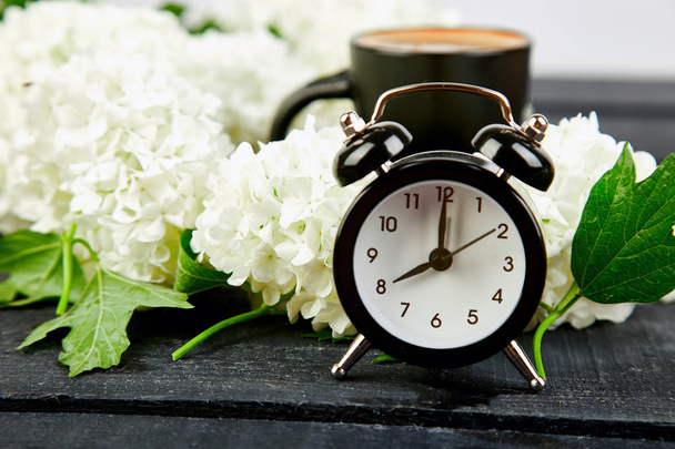 Black alarm clock and white flowers on black background.  Mother or Women Day. Greeting Card. Good Morning breakfast.  Spring. Romantic.  - Photo, Image