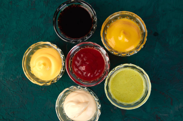 Set of different sauces. Sauces ketchup, mustard, mayonnaise, wasabi, soy sauce in little bowls on green background - Foto, imagen