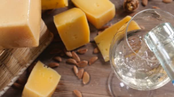 Víno a sýr. Jídlo umění. Různé druhy tvrdý sýr krásně surved na dřevěné pozadí. Bílé víno se nalije do sklenice na víno. - Záběry, video