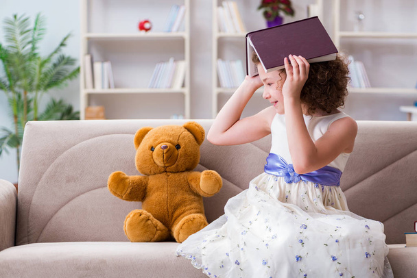 Маленькая симпатичная девочка читает дома книги - Фото, изображение