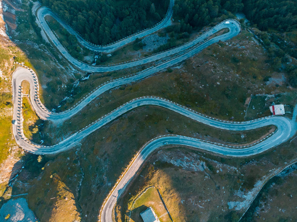 Aerial: top down view tailspin over winding mountain road on the Italian Alps, crossing green meadow and pasture in alpine valley, adventure road trip in summer.  - Photo, Image