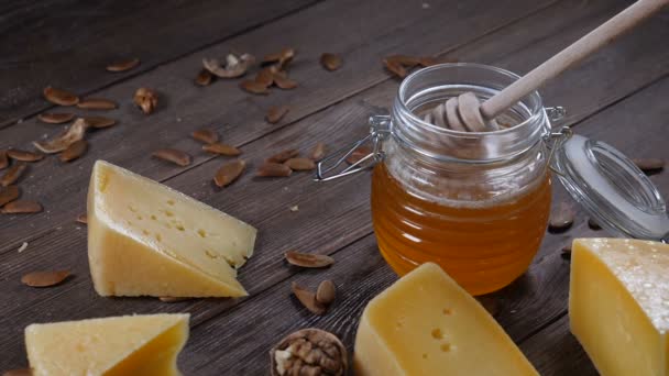 Cheese and honey. Variety of hard cheese is on wooden background. Honey on honey stick. Slow motion - Footage, Video