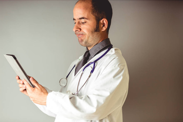 Ένας γιατρός με ένα στηθοσκόπιο γύρω από το λαιμό εξετάζει ένα δισκίο - Φωτογραφία, εικόνα