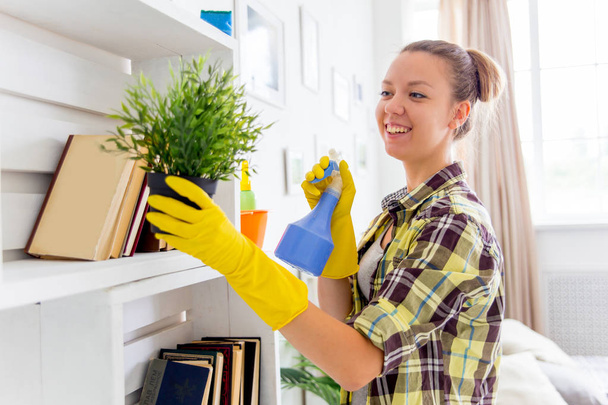 Woman in protective gloves is smiling and wiping dust using a spray and a duster - Foto, Imagem
