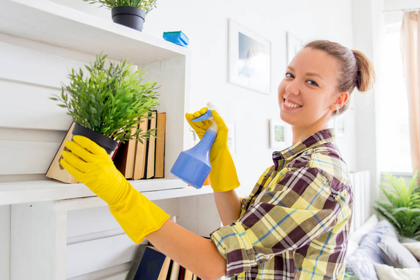 Frau in Schutzhandschuhen lächelt und wischt Staub mit Spray und Staubwedel ab, während sie ihr Haus putzt, Nahaufnahme - Foto, Bild