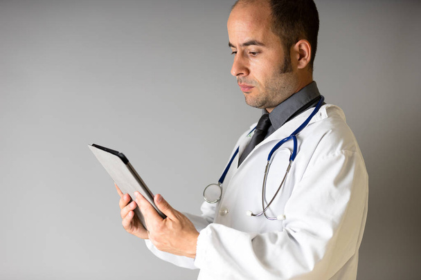 Ein Arzt mit einem Stethoskop um den Hals blickt auf eine Tablette - Foto, Bild