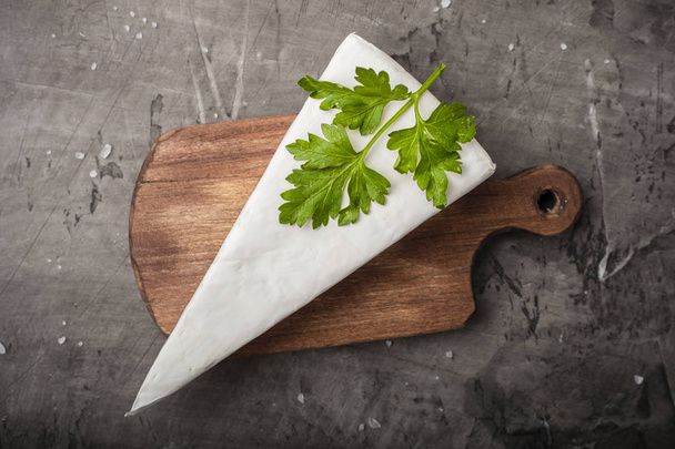 Soft cheese with white mold on a wooden cutting board. Decorated with green parsley   - Foto, afbeelding