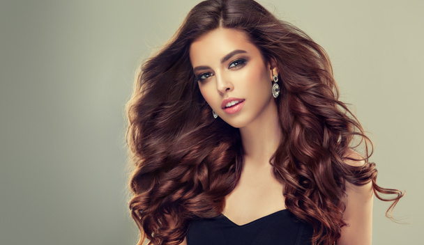 Brunette woman with long , healthy and shiny curly hair . Beautiful model girl with wavy hairstyle .Care and beauty products - Photo, Image
