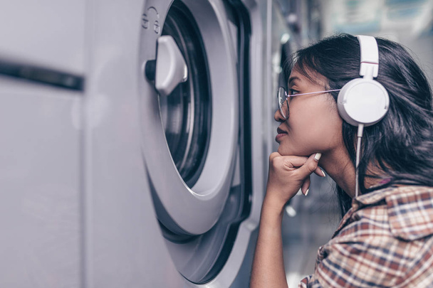 Jeune fille avec écouteurs à une machine à laver
 - Photo, image