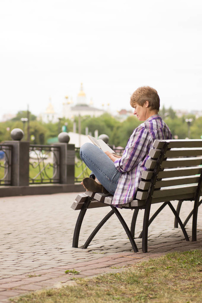 Счастливая женщина сидит и читает книгу на набережной
 - Фото, изображение