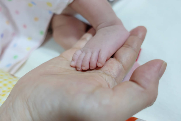 Close-up van moeder met voet van pasgeboren baby in haar hand. - Foto, afbeelding