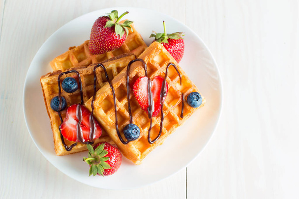Photo of fresh homemade food made of berry Belgian waffles with honey, chocolate, strawberry, blueberry, maple syrup and cream. Healthy dessert breakfast concept with juice.  - Foto, imagen