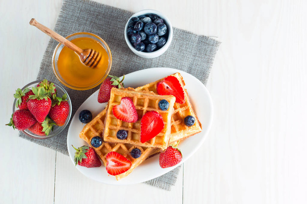 Photo of fresh homemade food made of berry Belgian waffles with honey, chocolate, strawberry, blueberry, maple syrup and cream. Healthy dessert breakfast concept with juice.  - Foto, Bild