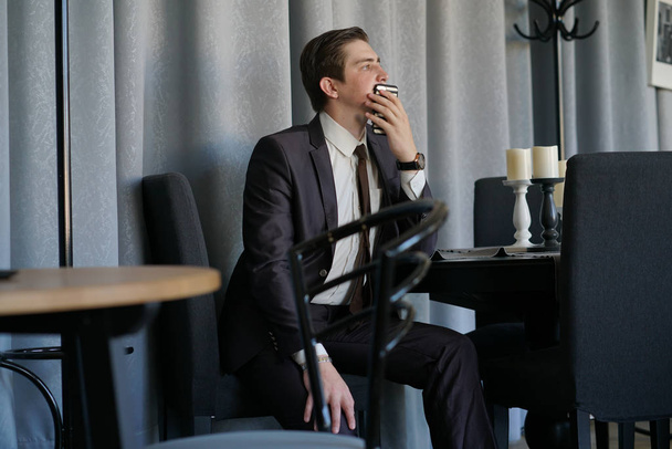 sad man in a business suit sitting with a phone in a cafe. he's upset. - Foto, immagini