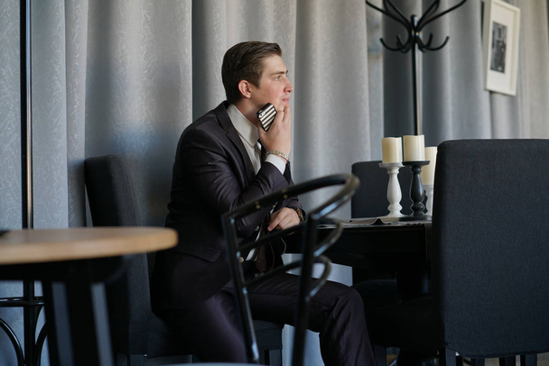um homem triste num fato de negócios sentado com um telefone num café. Ele está chateado.
. - Foto, Imagem